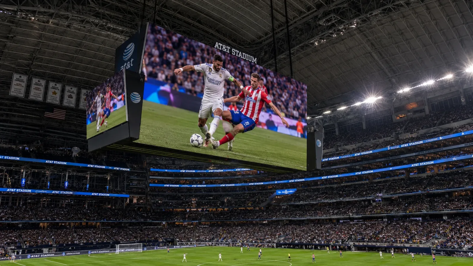 An internal photograph of AT&T Stadium focusing on the colossal hanging HD videoboard over the soccer field, highlighting its massive size.
