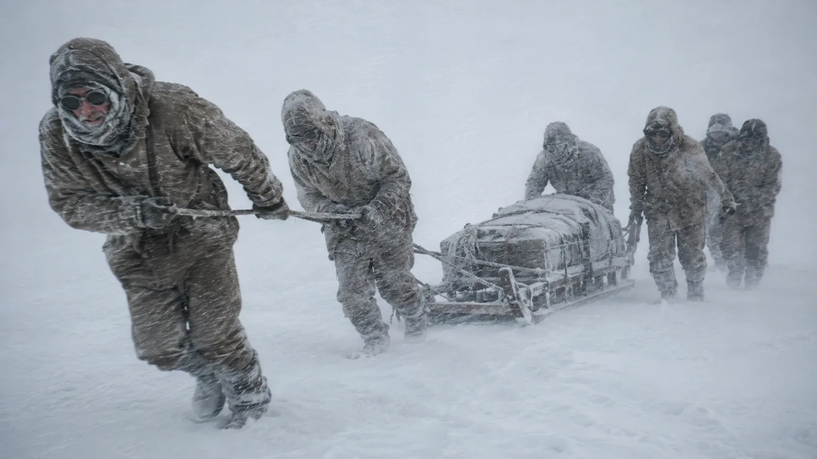 Exhausted polar explorers painfully pulling a heavy wooden sledge by hand through a blinding Antarctic snowstorm.
