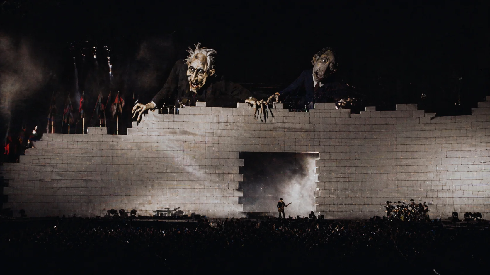 A high-quality photo from Pink Floyd's 1980 The Wall tour, showing the massive white wall under construction during the concert with towering inflatables.