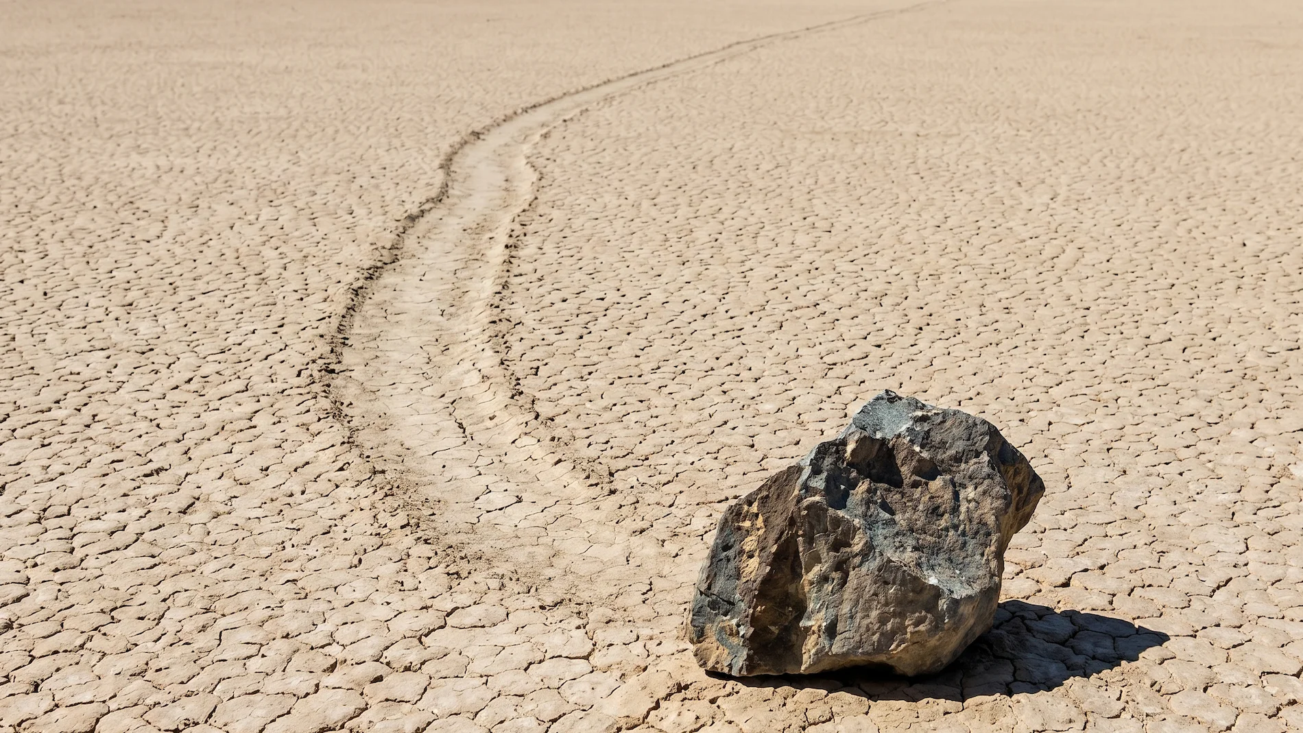 A mysterious sailing stone with its long trail on the cracked mud surface of Racetrack Playa in Death Valley.